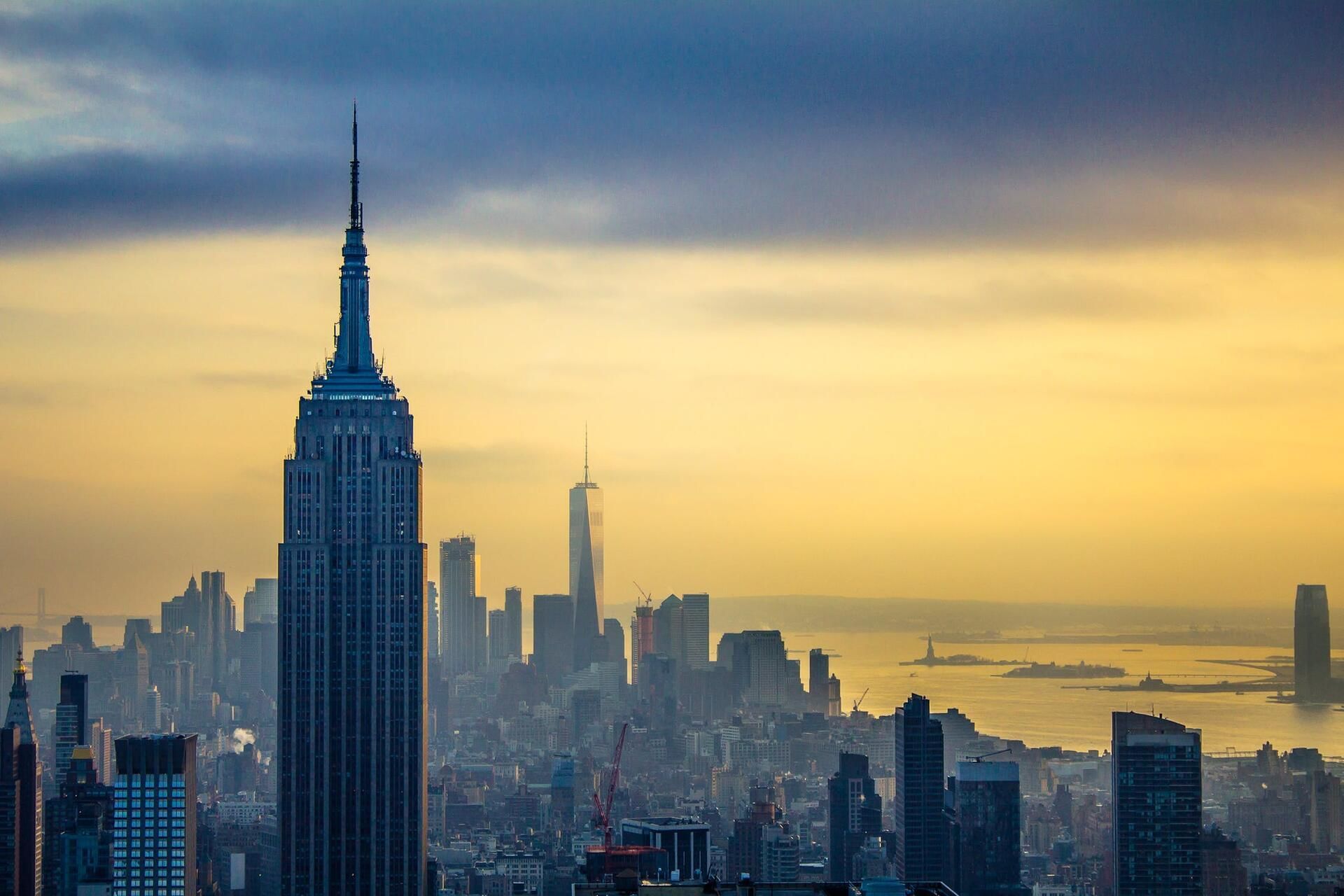A city skyline at sunset with skyscrapers and a body of water in the background.